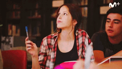 a girl in a plaid shirt is holding a blue pen in front of a m+ logo