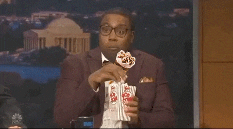 a man in a suit and bow tie is eating popcorn while wearing a face mask .