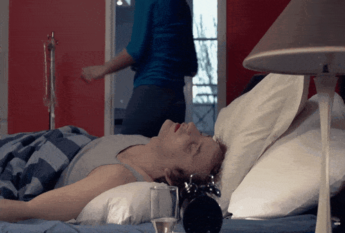a man laying on a bed with an alarm clock and a glass of water