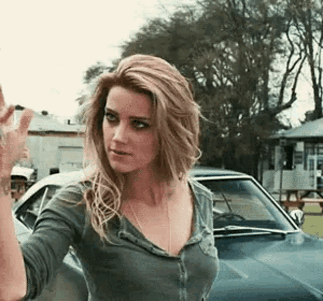 a woman in a gray shirt is standing in front of a car .