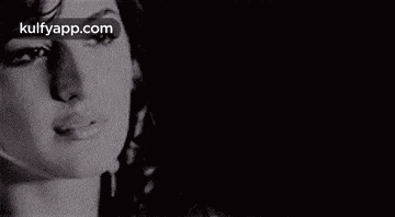 a close up of a woman 's face in a black and white photo with a black background .