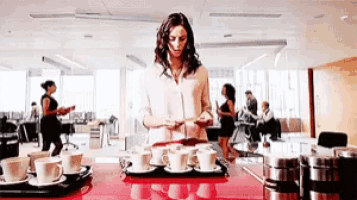 a woman stands in front of a tray of cups and saucers
