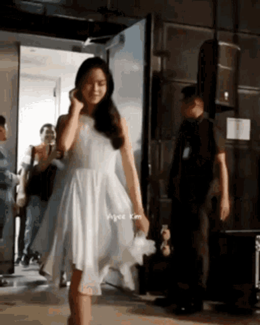 a woman in a white dress is walking through a doorway while a man stands behind her .
