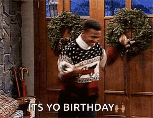 a man in a sweater is standing in front of a door holding a wreath and saying it 's yo birthday .