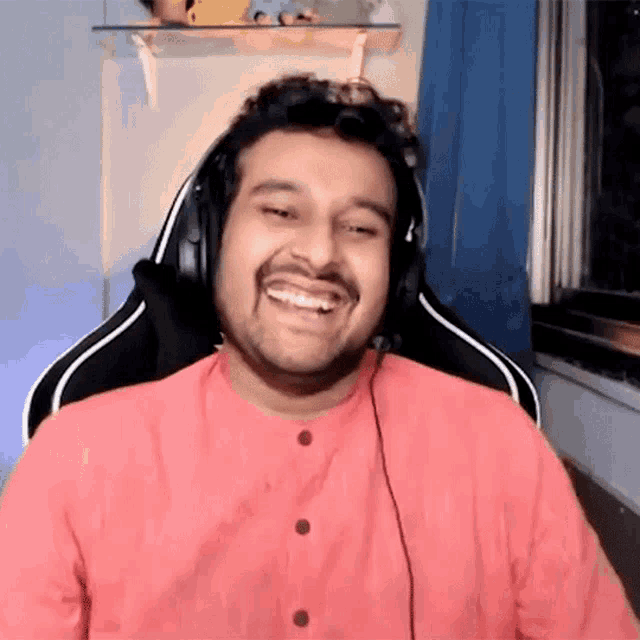 a man wearing headphones and a pink shirt is smiling .