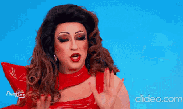 a drag queen wearing a red latex dress is waving her hand