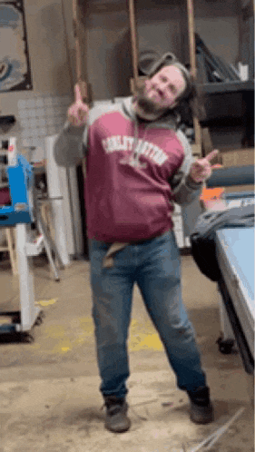a man in a red sweatshirt and blue jeans is standing in a room giving a thumbs up .