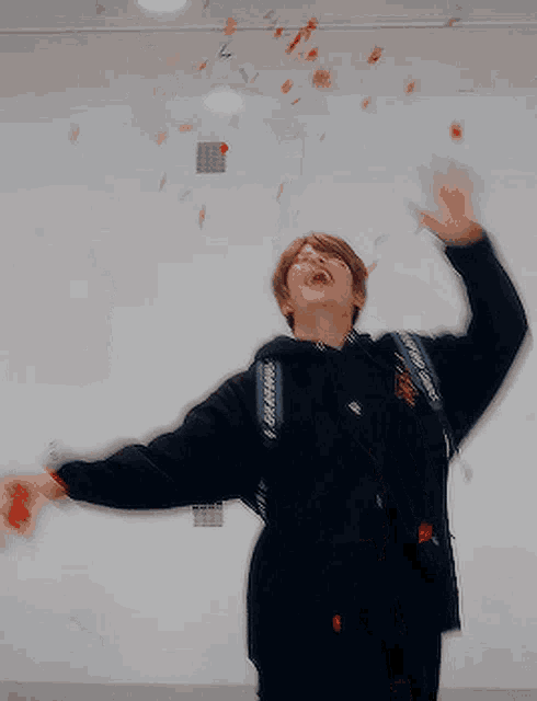 a man in a black jacket is throwing red confetti in the air