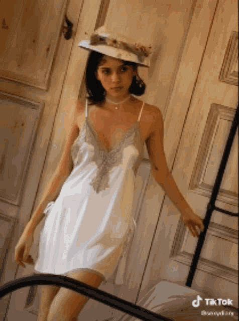 a woman wearing a white dress and a hat stands in front of a door