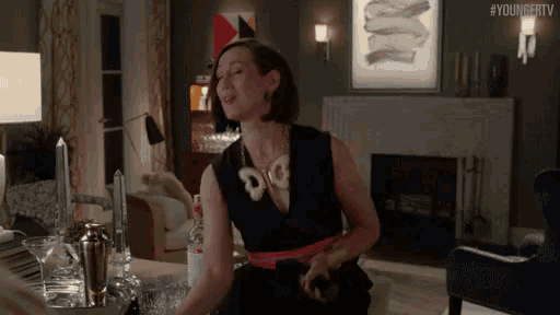 a woman in a black dress is sitting in a living room with #youngertv written on the bottom of the screen