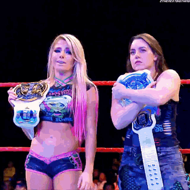 two women are standing in a wrestling ring holding their championship belts ..