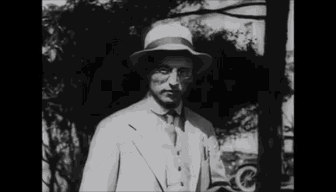 a man in a suit and hat stands in front of a tree