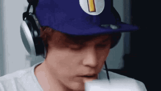a man wearing a purple hat and headphones is drinking milk from a glass .