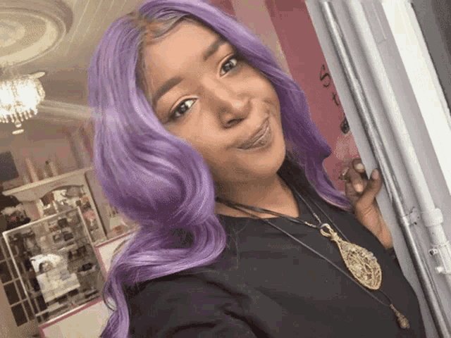 a woman with purple hair wearing a black shirt and a gold necklace
