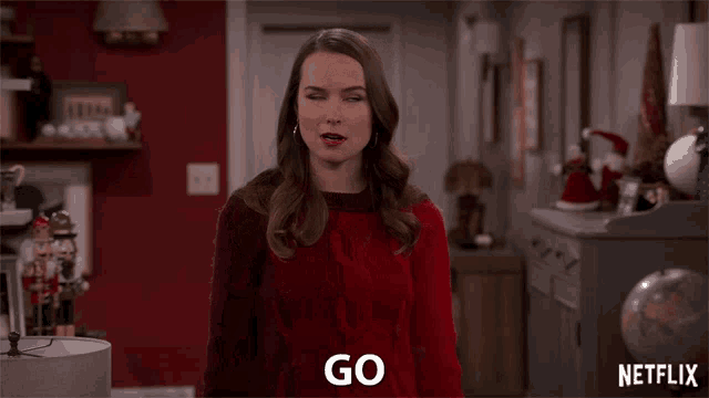 a woman in a red sweater is saying go in a living room