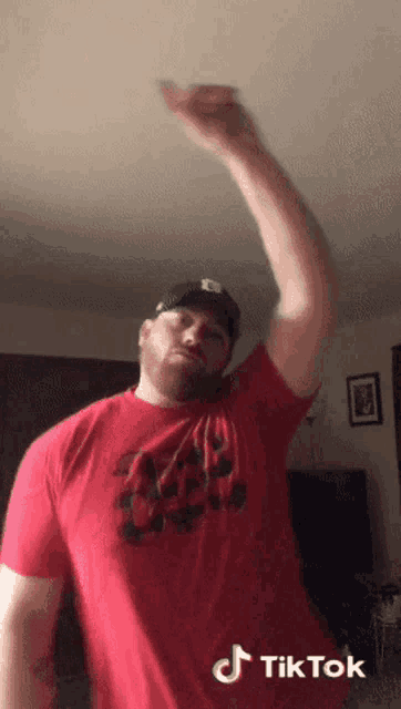 a man wearing a red shirt and a black hat has a tiktok sticker on his shoulder