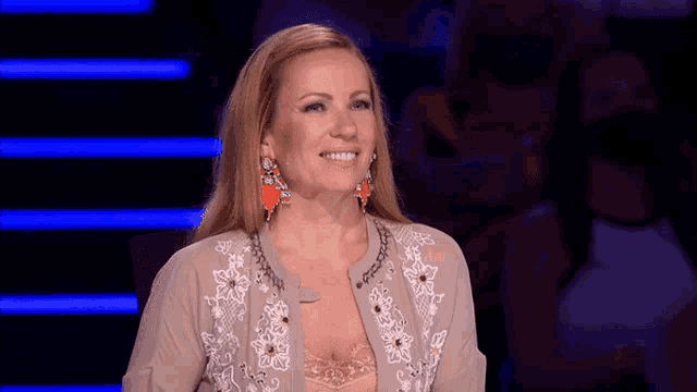 a woman wearing a cardigan and earrings is smiling