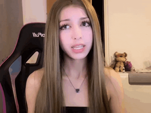 a woman with long blonde hair is wearing a necklace and sitting in front of a gaming chair that says iiu70 on it