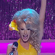 a drag queen is singing into a microphone while wearing a yellow top .