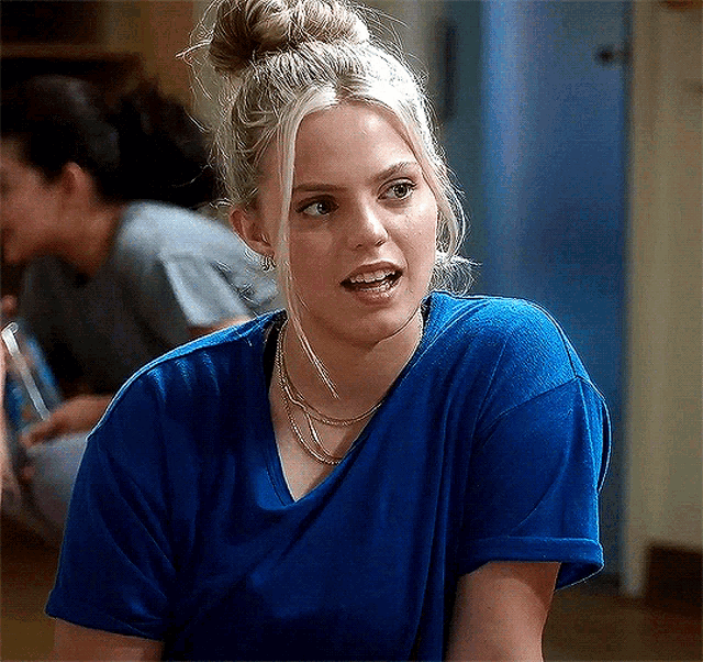 a woman wearing a blue t-shirt and a bun is sitting in a room .
