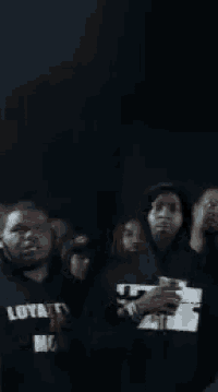 a group of men are standing in a dark room and one of them is wearing a shirt that says loyalty