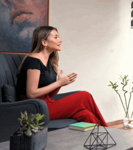 a woman in red pants is sitting on a couch talking