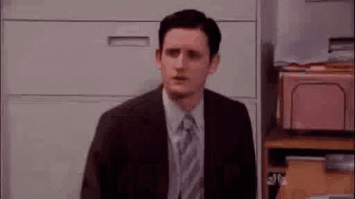 a man in a suit and tie is sitting at a desk in front of a filing cabinet .
