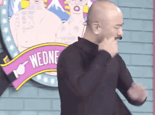 a bald man stands in front of a sign that says wedne