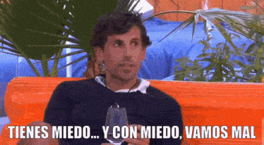 a man is sitting on an orange couch holding a wine glass and says tienes miedo