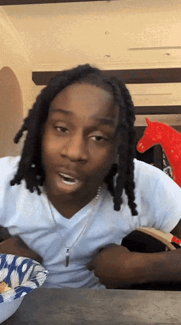 a man with dreadlocks sits at a table with a bowl of chips in front of him