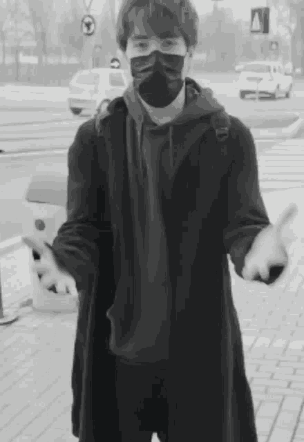 a black and white photo of a man wearing a face mask and a coat