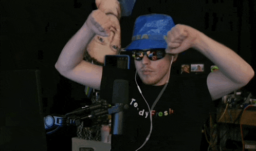 a man wearing a teddy fresh t-shirt and a blue hat stands in front of a microphone