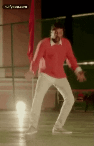 a man in a red shirt and white pants is dancing in a gym .