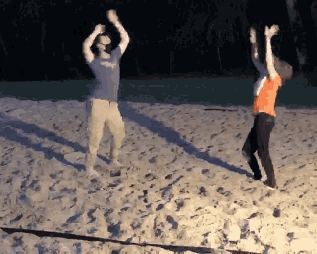 two people are jumping in the air on a sandy beach at night