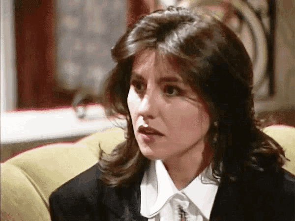 a woman in a black suit and white shirt is sitting on a yellow couch