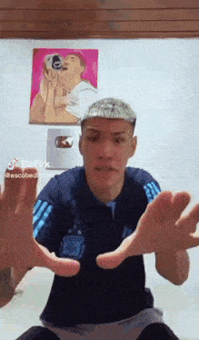 a man in a blue shirt is making a funny face with his hands outstretched in front of a painting .