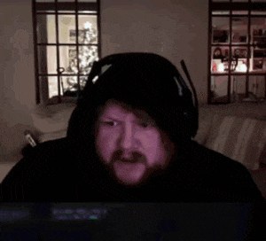 a man with a beard wearing headphones and a hooded jacket is laying in a bed .