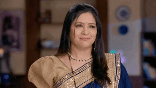 a woman in a blue and gold saree smiles at the camera