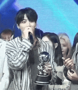 a man is holding a trophy and singing into a microphone while standing in front of a crowd .