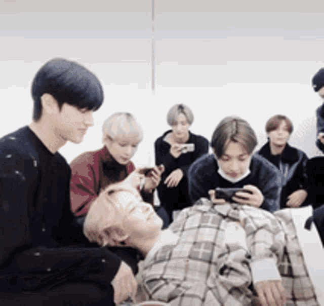 a group of young men are sitting around a person laying on the floor looking at a cell phone .