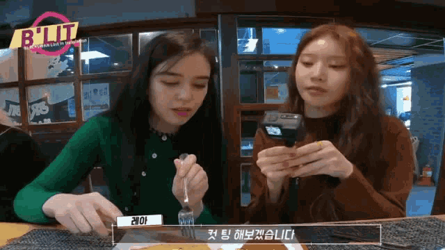 two girls sitting at a table with a sign that says but on it