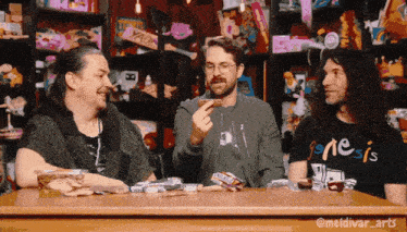 three men are sitting at a table with one wearing a shirt that says genesis