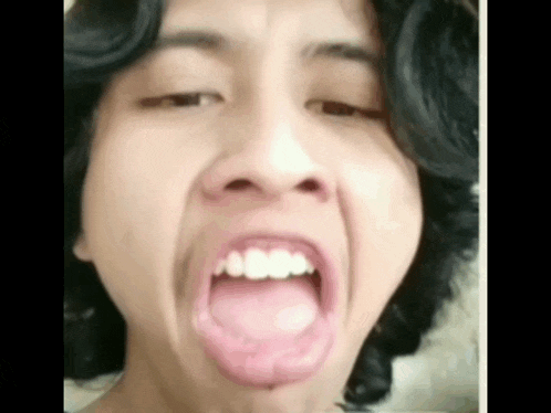 a young man with long hair is making a funny face with his mouth open .