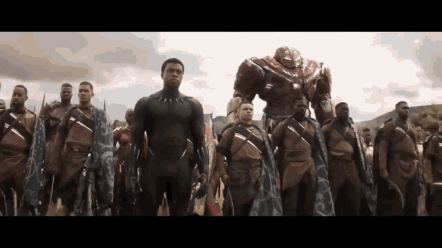 a man in a black suit is standing in front of a group of men in armor .