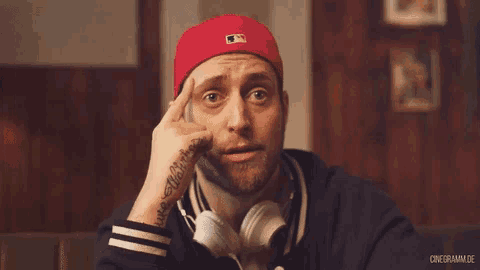 a man wearing headphones and a red hat has a tattoo on his wrist that says ' always ' on it