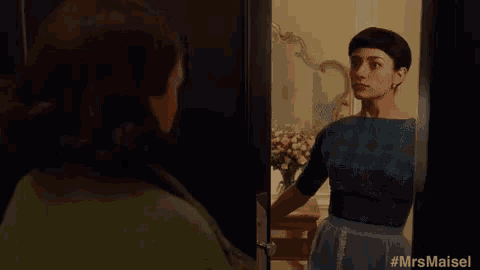 a woman in an apron is standing in front of a door looking at herself in the mirror .