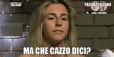 a woman is standing in front of a brick wall with the words ma che cazzo dici