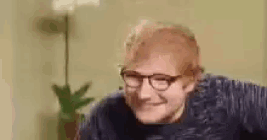 a man wearing glasses and a blue sweater is smiling .
