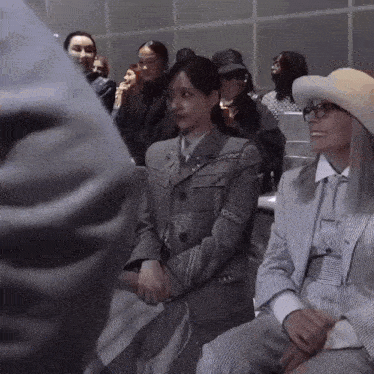 a woman in a suit is sitting next to a woman in a hat .