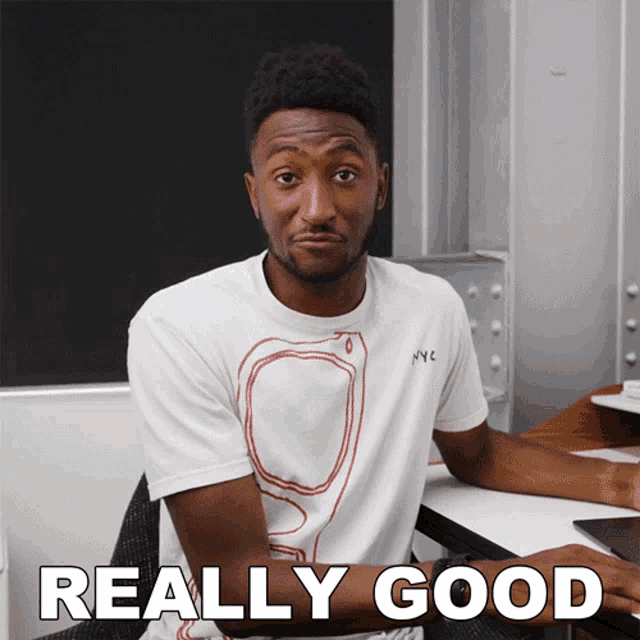 a man in a white shirt is sitting at a desk with the words really good written on his arm